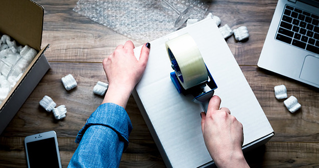 5 Reasons Self-Storage Investing Will Continue Its Incredible Run woman packing and sealing a moving box with tape