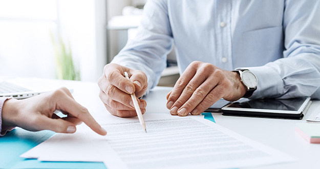There’s a 90% Chance You Have the Wrong Insurance Policy closeup of two people going over business documents fanned out on desk and pointing to line items with finger and pencil