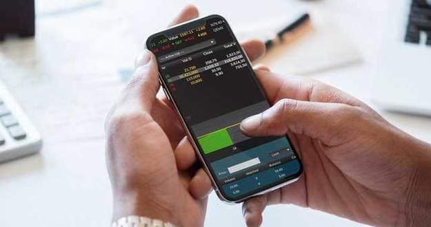 Real Estate Over Stocks? Making a Case for Real Estate Investing closeup of man holding smart phone checking stocks