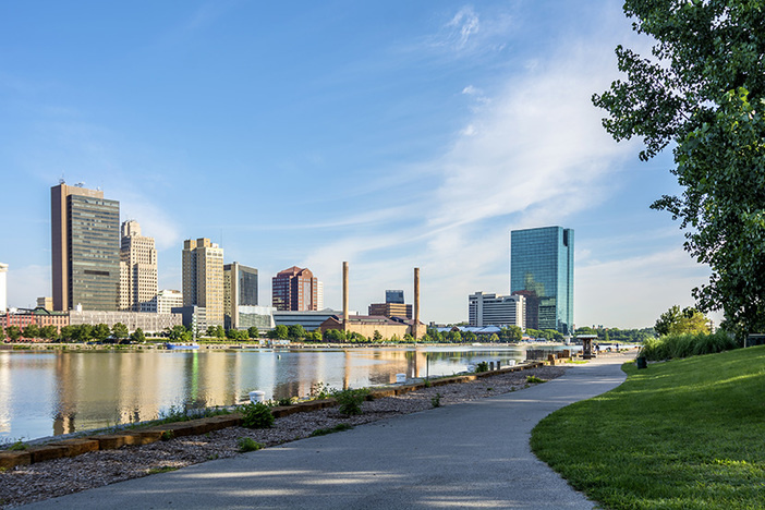 The No. 1 Most Overlooked Real Estate Market (Are YOU Missing Out?!) A panoramic view of downtown Toledo Ohio's skyline from across the Maumee river at a popular local park. A beautiful blue sky with white clouds for a backdrop.