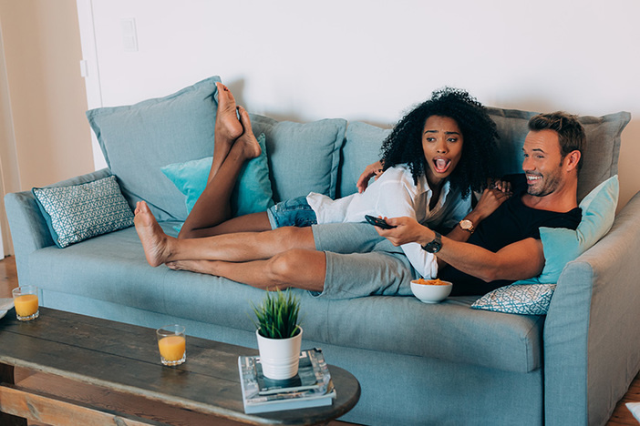 Why Your “Bachelorette”-Loving Spouse Could Unexpectedly Catch the Real Estate Bug Happy young couple relaxed at home in the couch having fun watching tv