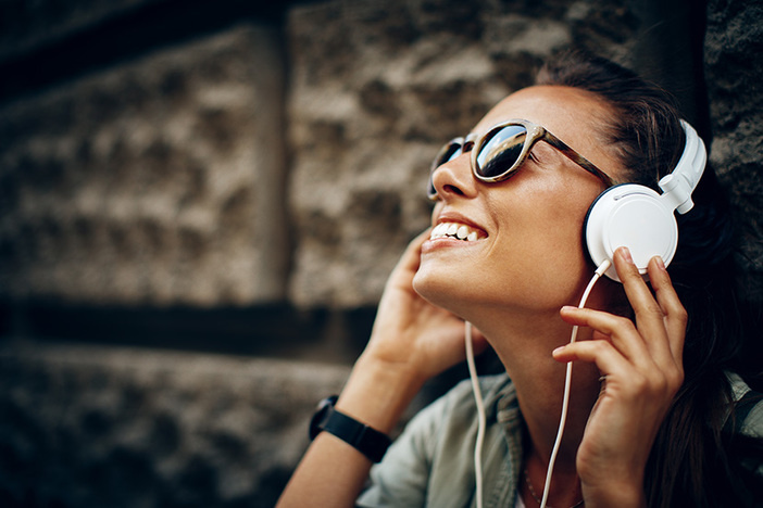 Top 5 Podcasts for Multifamily Real Estate Investors smiling dark haired girl listening to white headphones and smiling sitting outside in urban setting