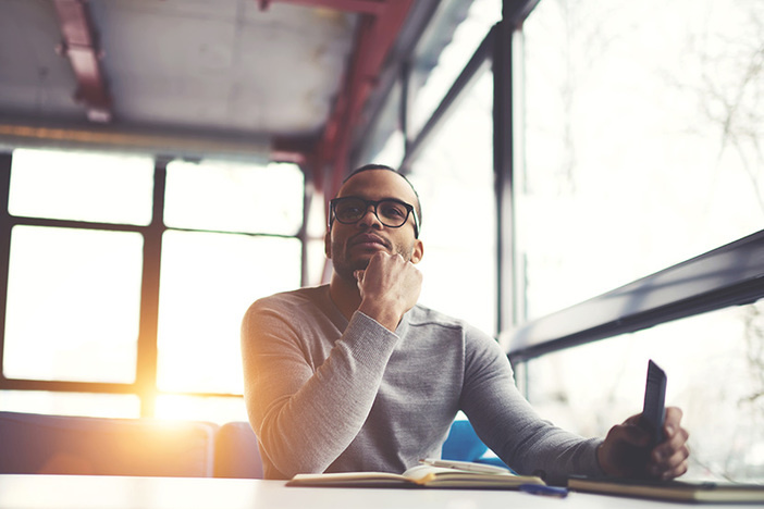 How to Win in Today’s Economy Pensive afro american handsome professional writer of popular articles in blog dressed in trendy outfit and glasses thinking over new story proofreading his script from notebook sitting in cafe