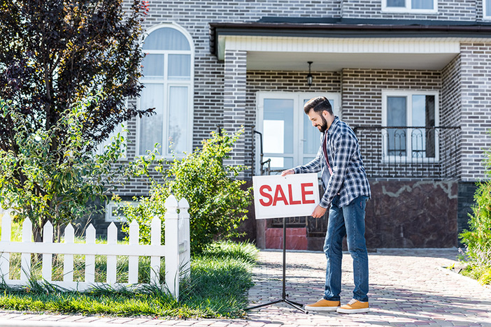 Plan to Sell Your Primary Residence? STOP… And Consider This First. young man placing sale sign in front of his house