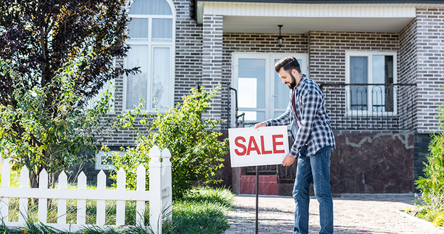 Plan to Sell Your Primary Residence? STOP… And Consider This First. young man placing sale sign in front of his house