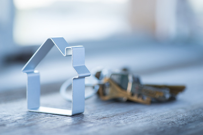 How to Retire in 3 Years Through Real Estate Investing cookie cutter of house on a table with blurred keys in the background