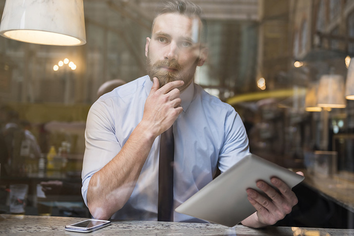 Creative Financing: 5 Outside-the-Box Tools Savvy Investors Use to Build Wealth white main behind window sitting at table with phone and tablet and inquisitive expression