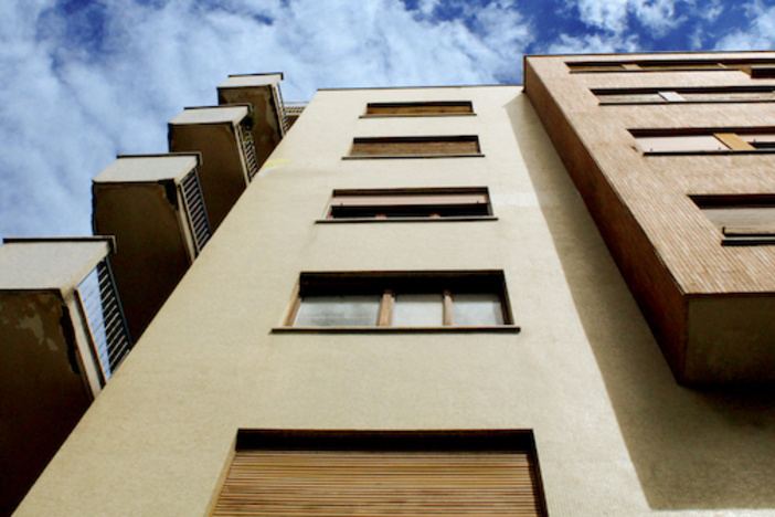 Single Family Homes vs. Multi-Unit Apartments: Which Investment is Right for You? looking up at a multilevel apartment building from the ground blue sky with clouds in backdrop